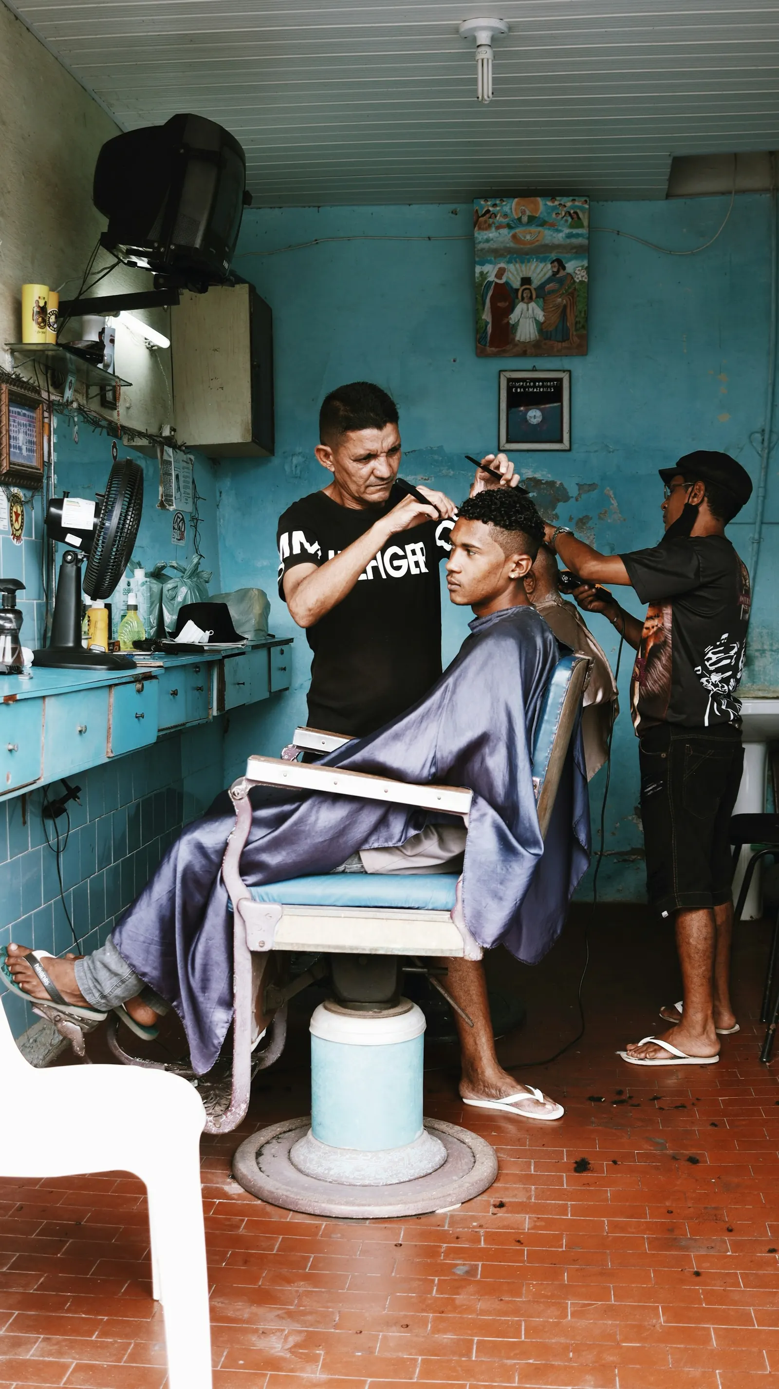 Barbers at work in a neighborhood shop with blue walls.