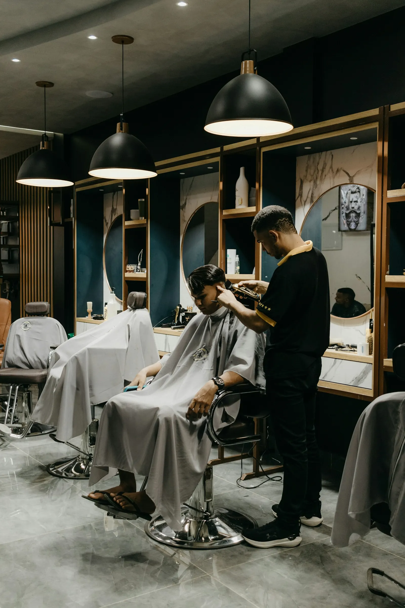 A barber shaping a client’s haircut in a shop with wood-framed mirrors.